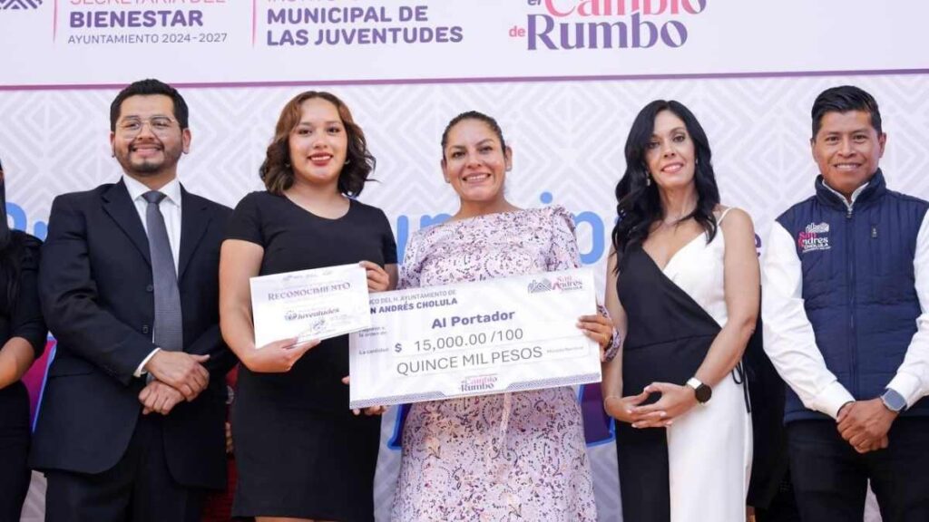 Dos mujeres sostienen un reconocimiento y un cheque simbólico de 15 mil pesos.