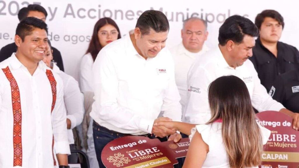 El gobernador de Puebla, Alejandro Armenta, aparece estrechando la mano de una mujer que sostiene una llave simbólica del centro asignado a su municipio, como acto representativo de la inauguración.